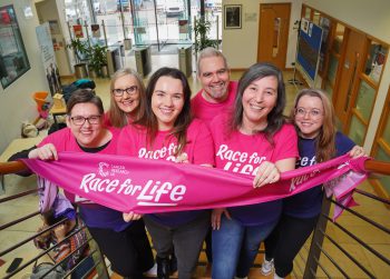 Six members of Belfast Experimental Cancer Medicine Centre hold banner to support Cancer Research UK Race for Life Event