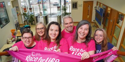 Six members of Belfast Experimental Cancer Medicine Centre hold banner to support Cancer Research UK Race for Life Event