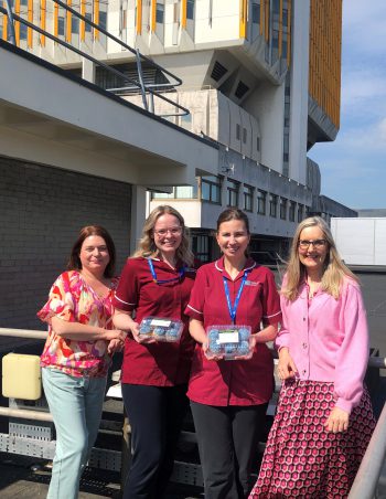 Four research nurses standing outside Belfast City Hospital with cupcakes to celebrate International Nurses Day