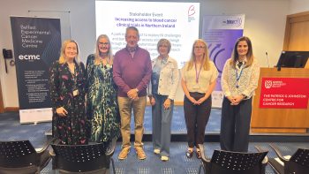 Image of people standing in front of a PowerPoint presentation at a Stakeholder event: Dr Sarah Lawless, Ms Ruth Boyd, Mr David Hetherington, Mrs Heather Hetherington, Dr Oonagh Sheehy and Aileen Major