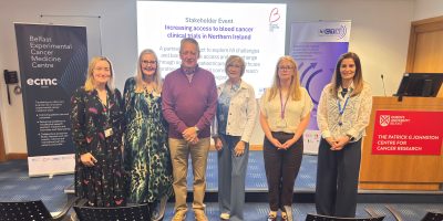 Image of people standing in front of a PowerPoint presentation at a Stakeholder event: Dr Sarah Lawless, Ms Ruth Boyd, Mr David Hetherington, Mrs Heather Hetherington, Dr Oonagh Sheehy and Aileen Major